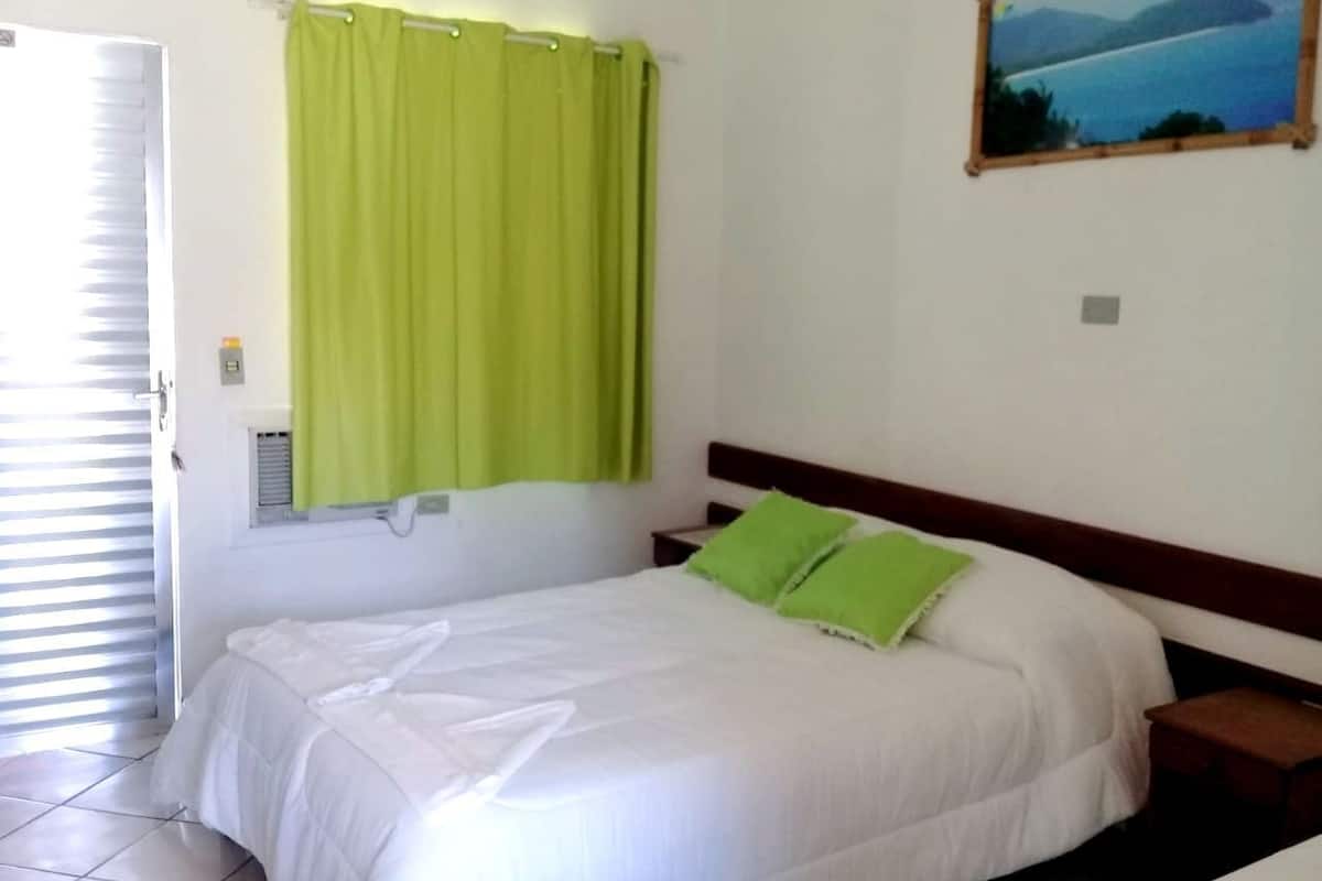 Ein Schlafzimmer mit einem Bett, grünen Vorhängen, einem Nachttisch und einem Wandbild.