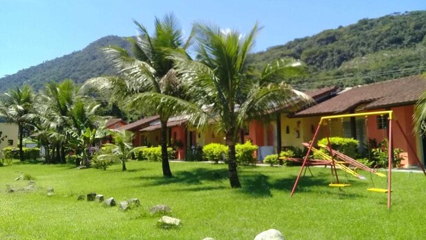Un hotel con fachada roja y amarilla, rodeado de abundante vegetación y palmeras.