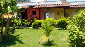 Un edificio con puerta roja, paneles solares en el techo y un jardín bien cuidado con diversas plantas.