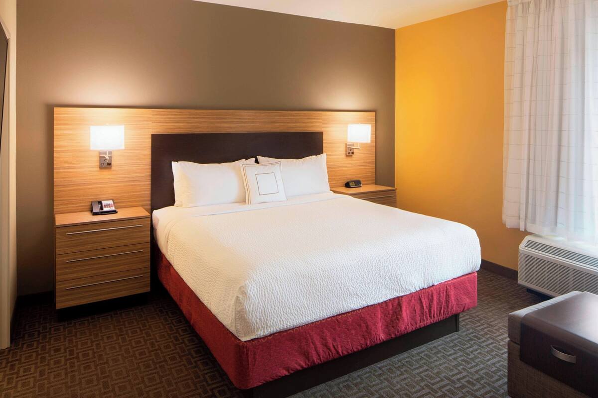 A hotel room with a large bed, two bedside tables, a nightstand, a desk, and a window with curtains.