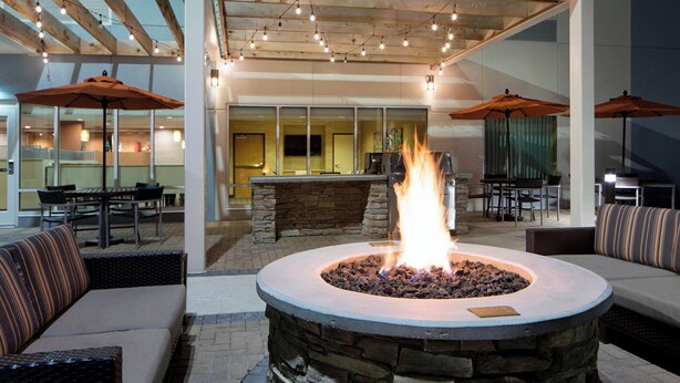 An outdoor patio area with a stone fire pit, wicker furniture, and umbrellas. - TownePlace Suites by Marriott Austin Round Rock (Austin)