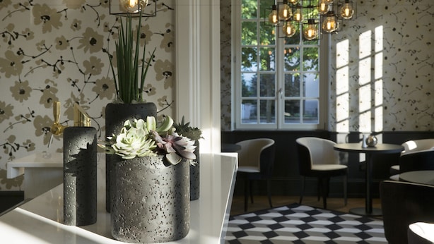 Ein modernes Interieur mit floralem Wandpapier, einem schwarz-weiß karierten Boden und einem Essbereich mit Stühlen und Tisch.