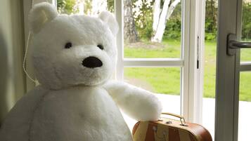 Un ours en peluche blanc est posé à côté d’une valise ancienne, près d’une fenêtre.