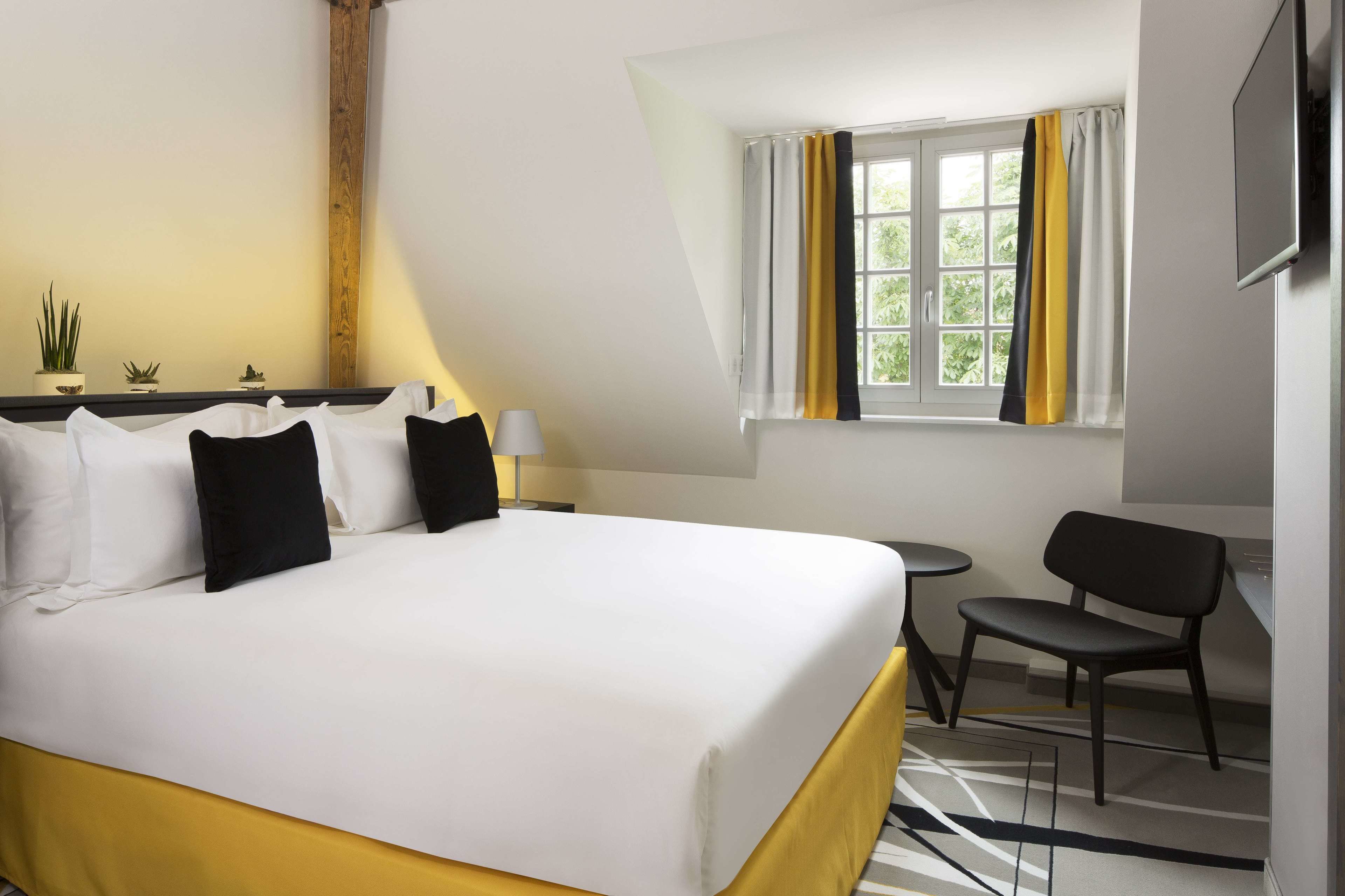 Une chambre d’hôtel avec un grand lit, une petite table, une chaise et une fenêtre avec des rideaux.
