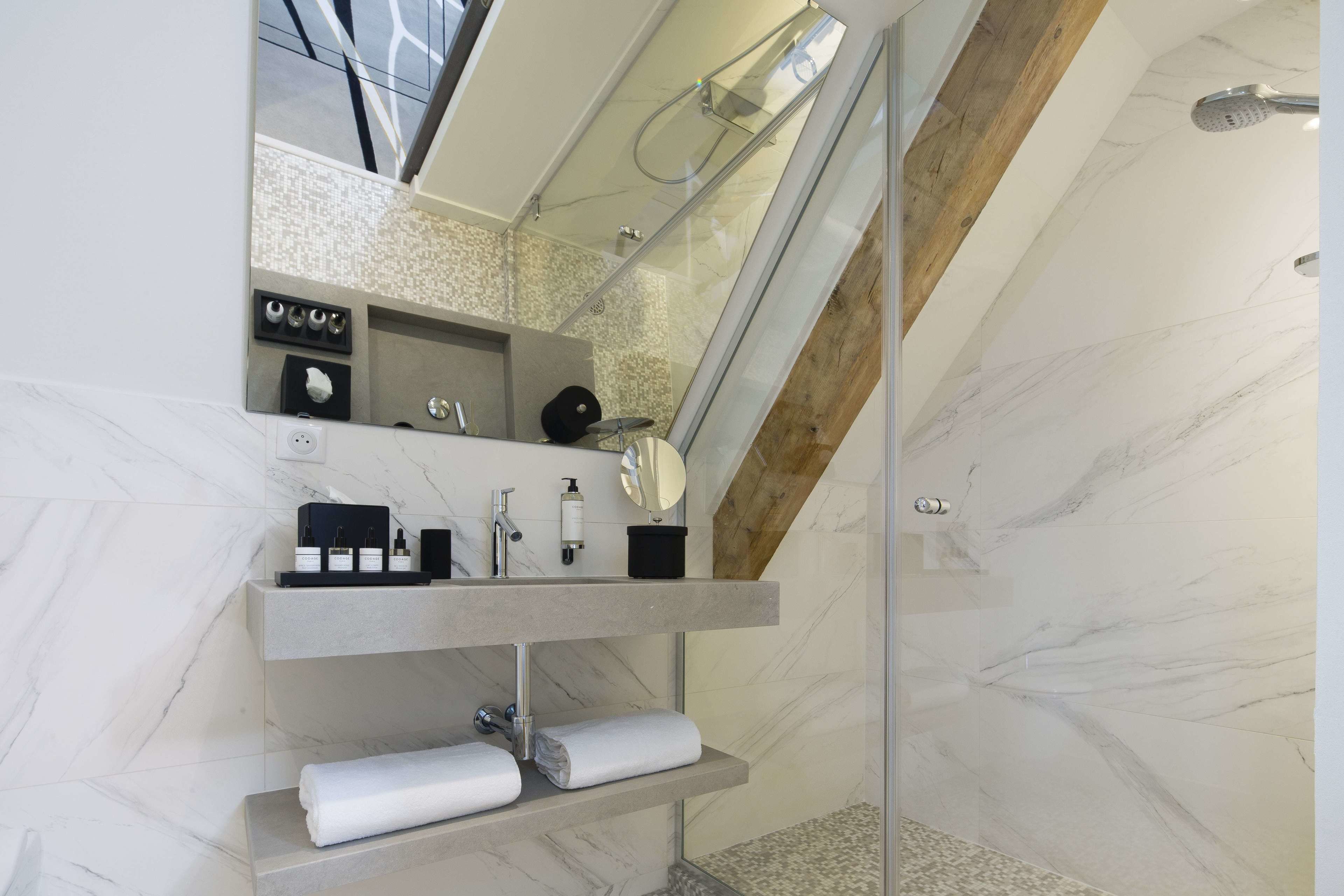 A modern bathroom with a glass-enclosed shower, marble walls, and a built-in vanity with a mirror and towel racks.
