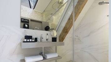 A modern bathroom with a glass-enclosed shower, marble walls, and a built-in vanity with a mirror and towel racks.