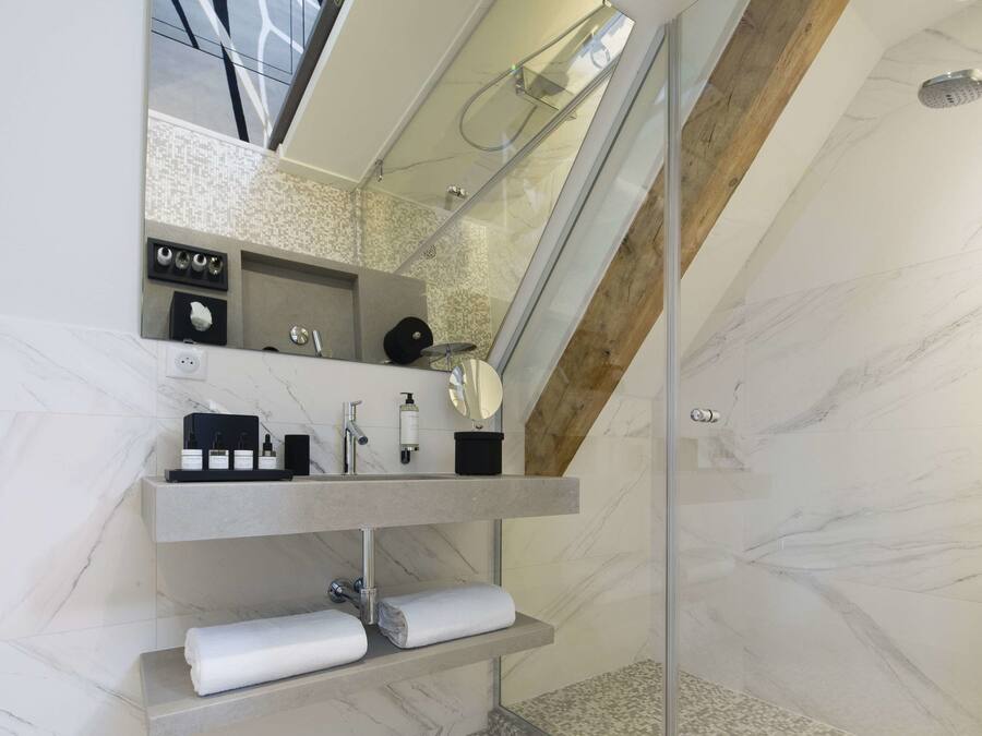 A modern bathroom with a glass-enclosed shower, marble walls, and a built-in vanity with a mirror and towel racks.