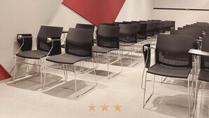 Un salón de conferencias en el Verona Tower Hotel, con filas de sillas negras y una pared decorativa roja.