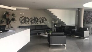 A modern lobby with a reception desk, black sofas, a staircase, and decorative wall art. - Hotel Verona Tower (Divinopolis)