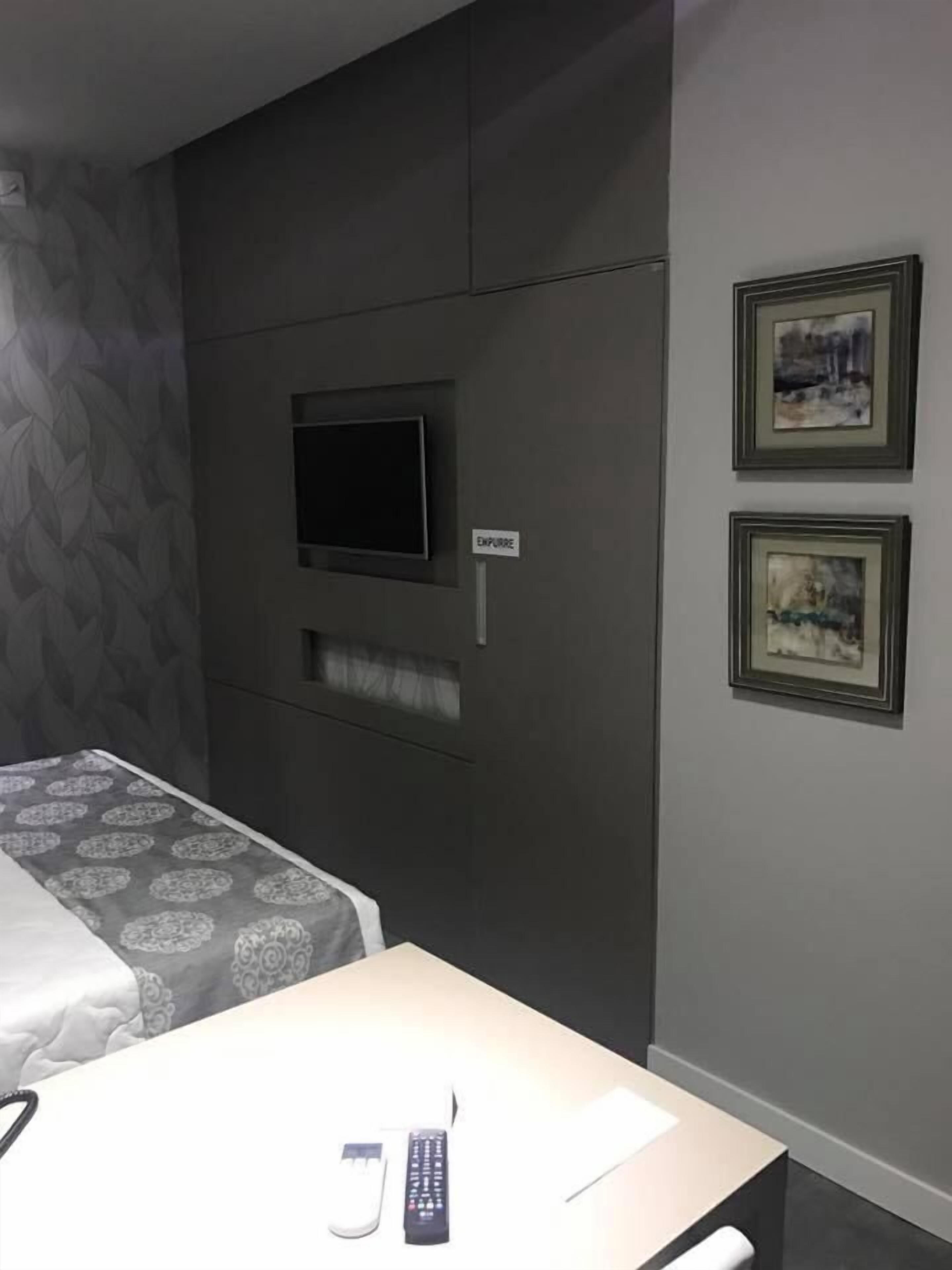 Una habitación de hotel con una cama, un televisor montado en la pared y dos cuadros enmarcados.