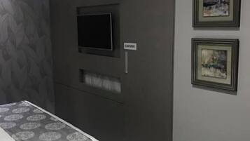 Una habitación de hotel con una cama, un televisor montado en la pared y dos cuadros enmarcados.