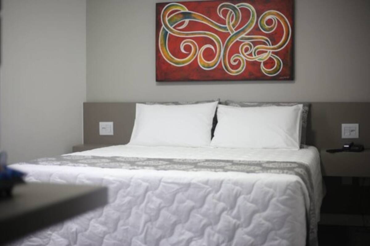 A hotel room with a bed, a nightstand, and a wall-mounted artwork.