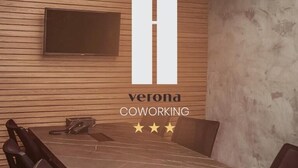Una sala de reuniones moderna con un panel de pared de madera, un televisor montado y el logotipo de 'verona coworking' con tres estrellas.