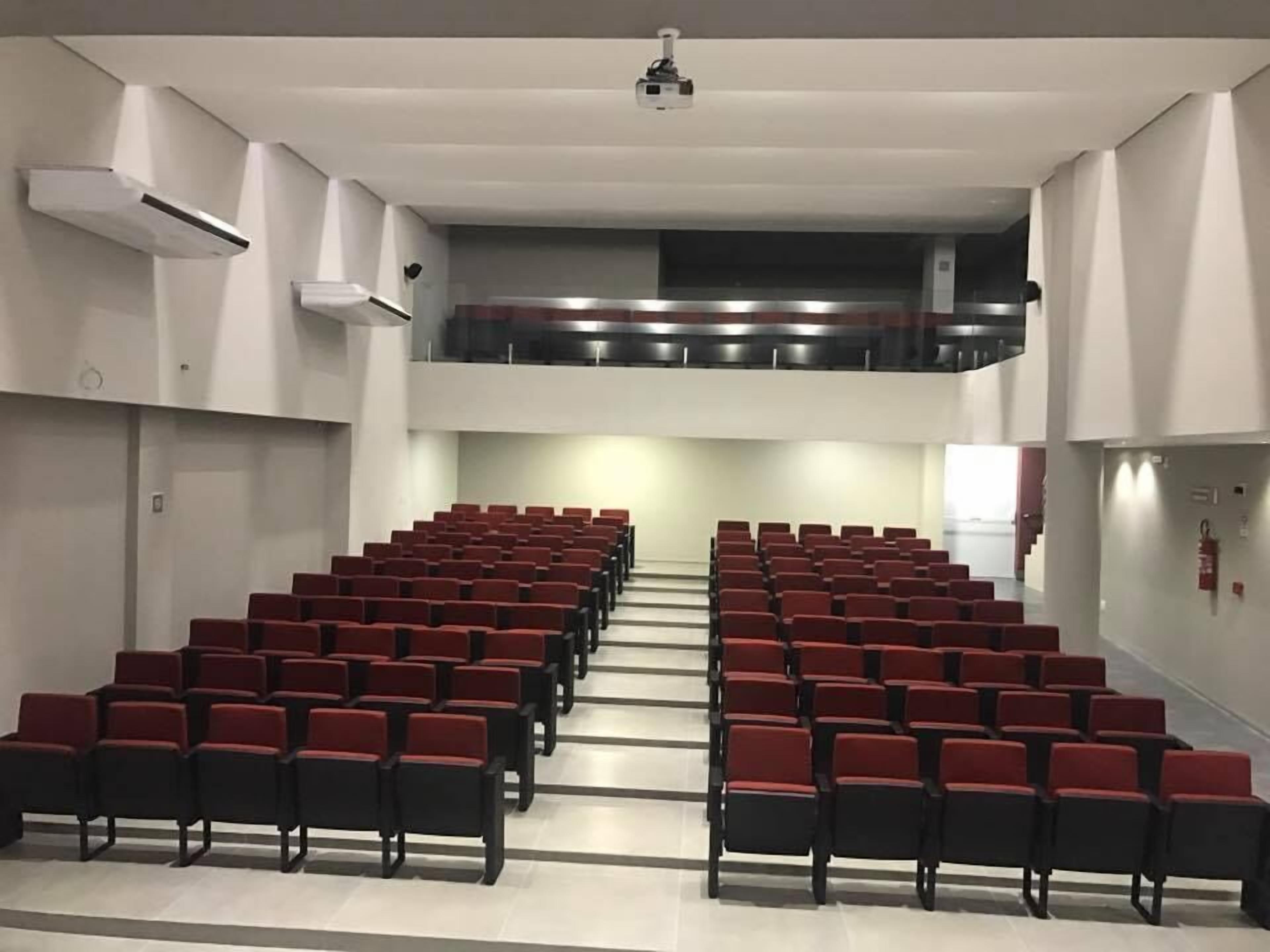 A large auditorium with rows of red chairs and a balcony.