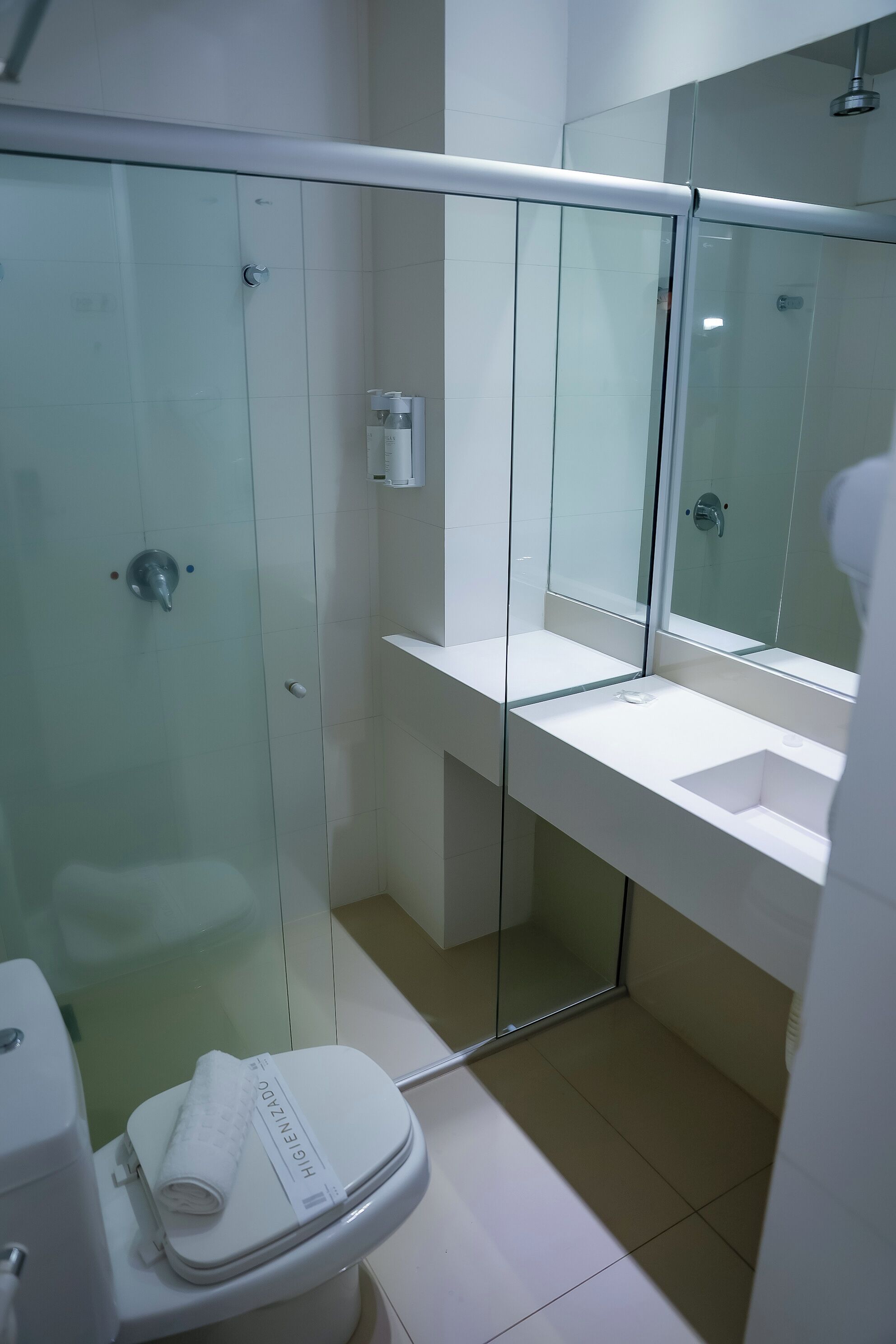 Un baño moderno con ducha envuelta en vidrio, un lavamanos blanco y un inodoro con una toalla.