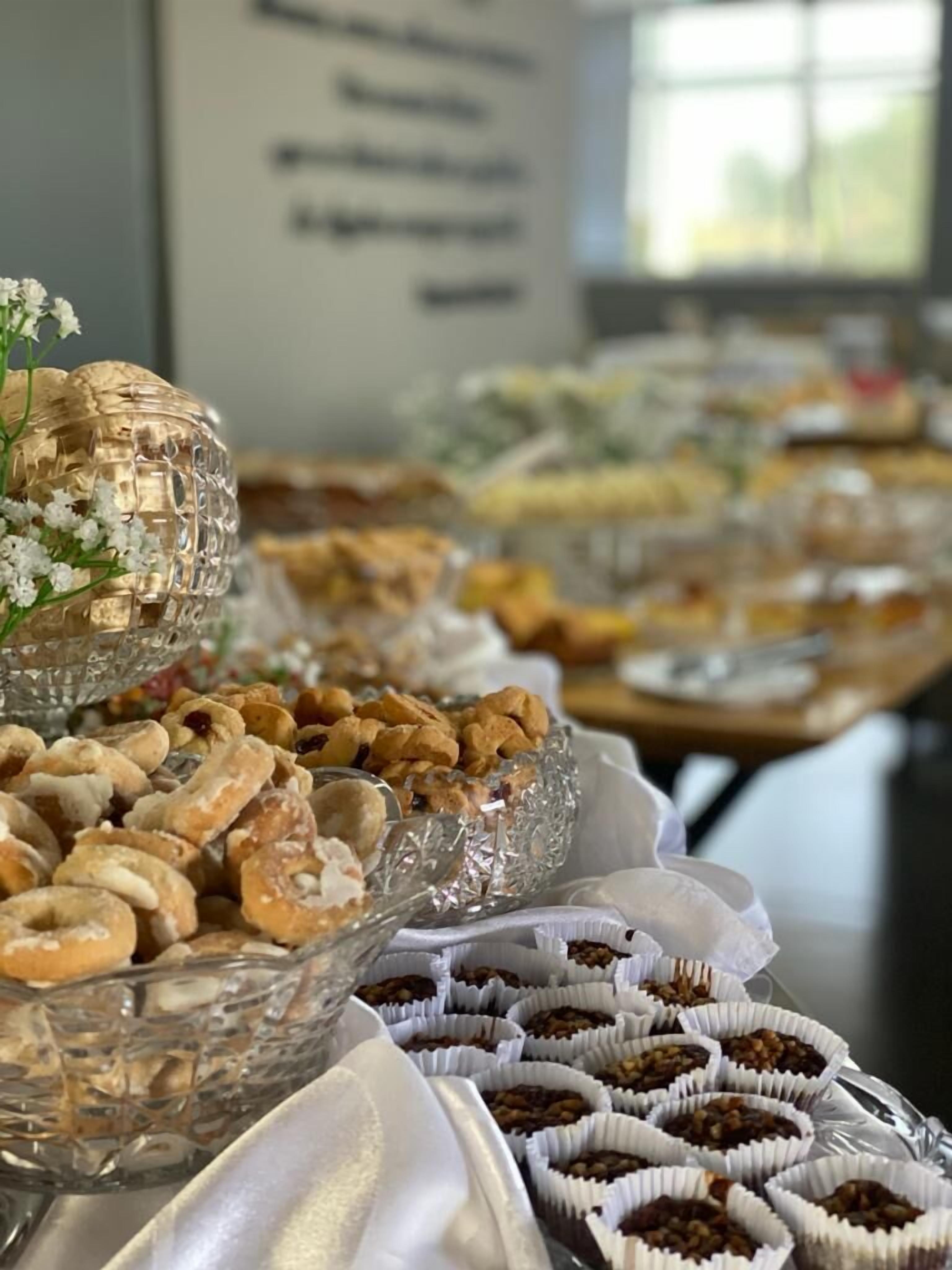 Una mesa de buffet con diversos alimentos, como pasteles y frutos secos, dispuestos en recipientes de vidrio y vasos de papel.