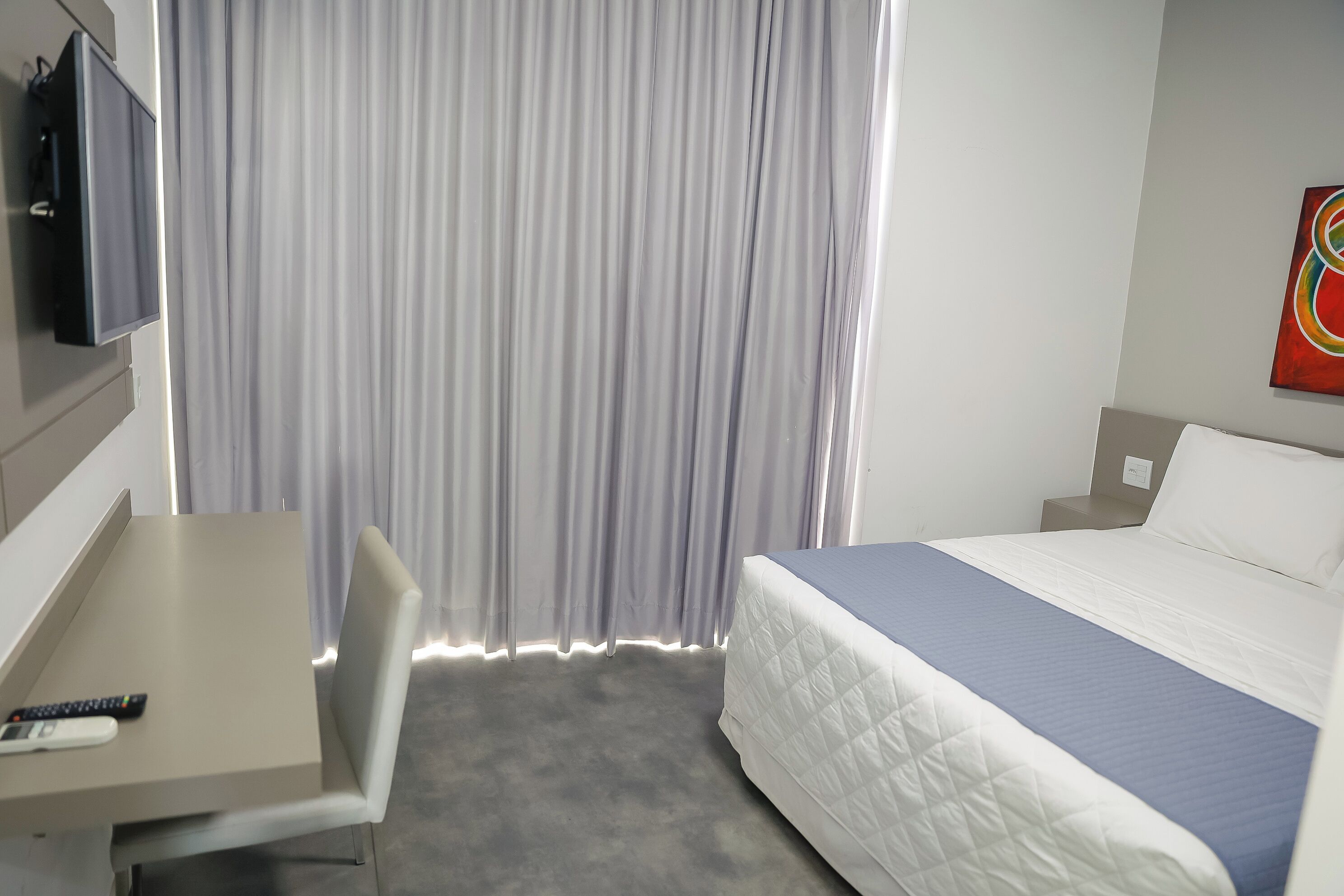 Habitación de hotel con cama, escritorio, silla, televisor y cortinas.