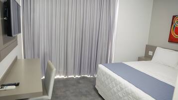 Habitación de hotel con cama, escritorio, silla, televisor y cortinas.
