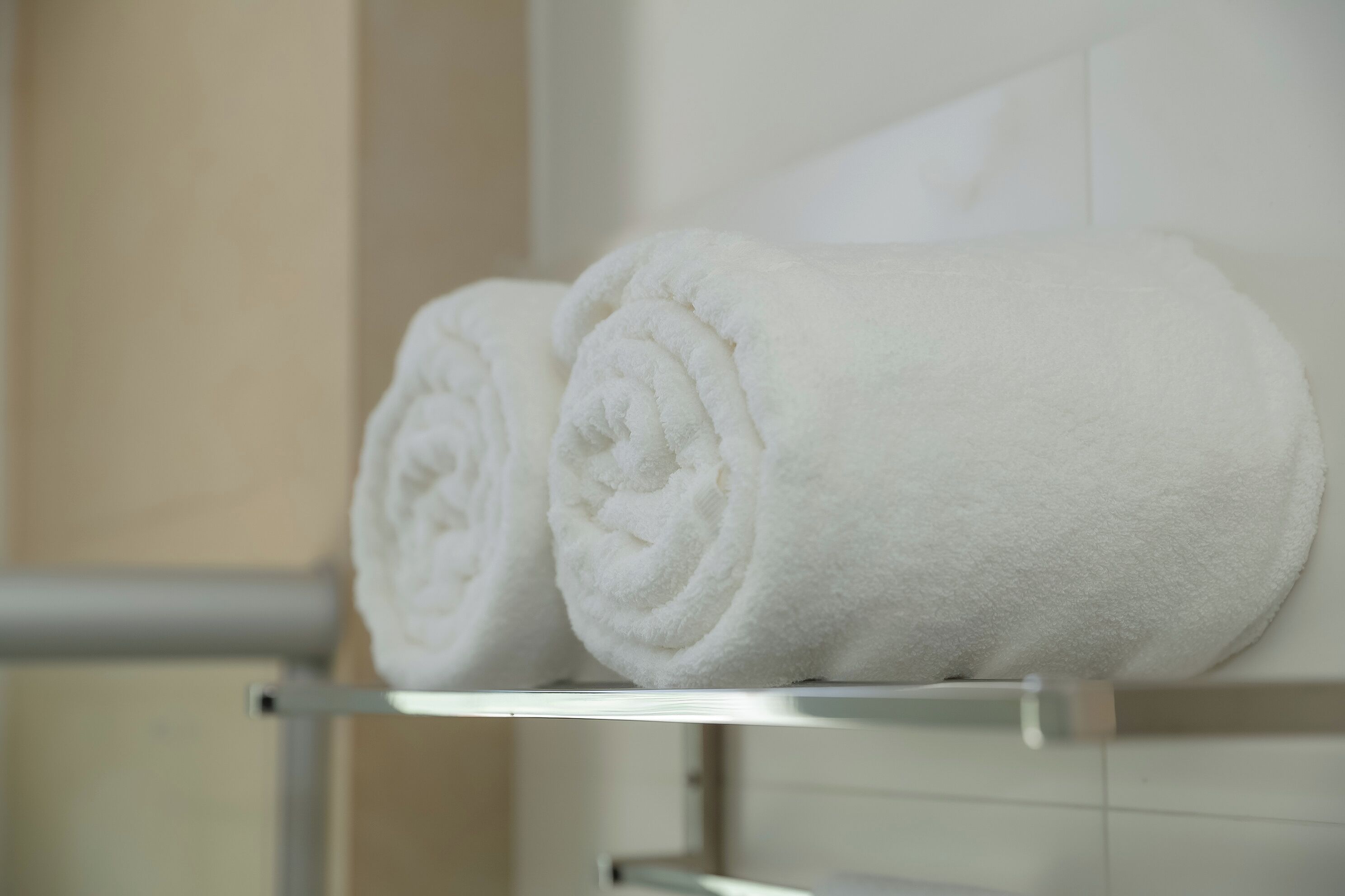 Two neatly rolled white towels on a metal shelf in a bathroom.