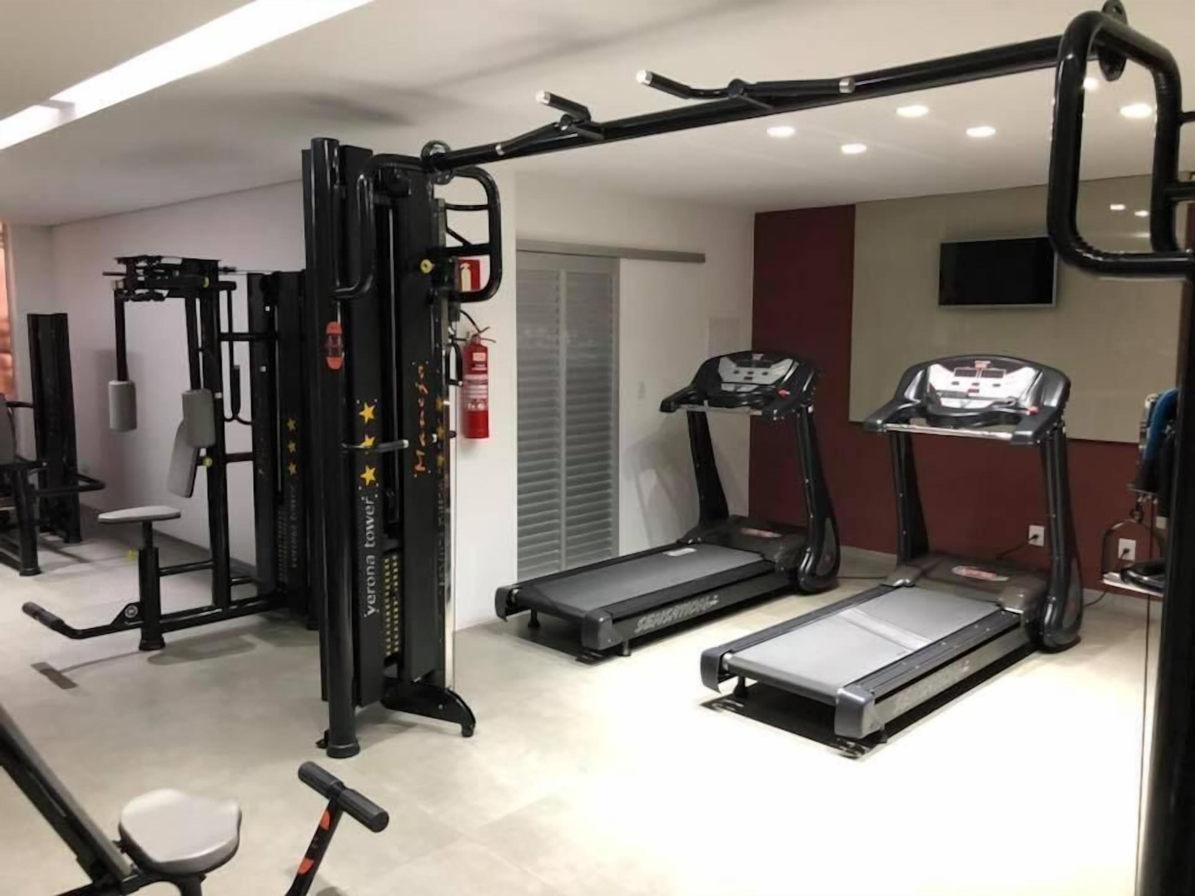 Uma academia com esteiras, uma máquina de musculação e uma barra para puxar.