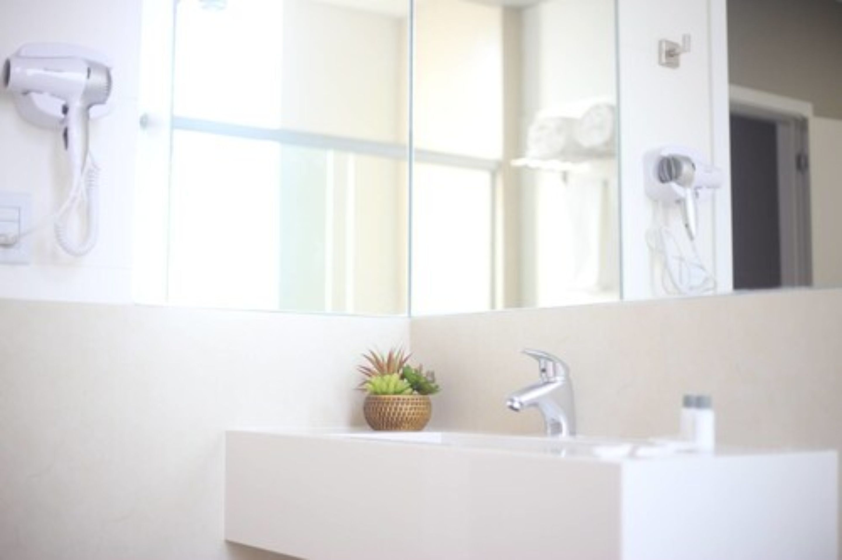 Un baño con un lavabo blanco, un espejo y un secador de pelo montado en la pared.