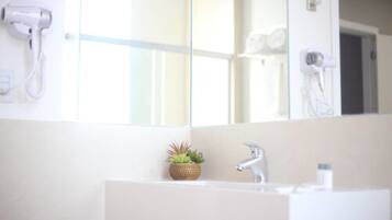 Un baño con un lavabo blanco, un espejo y un secador de pelo montado en la pared.
