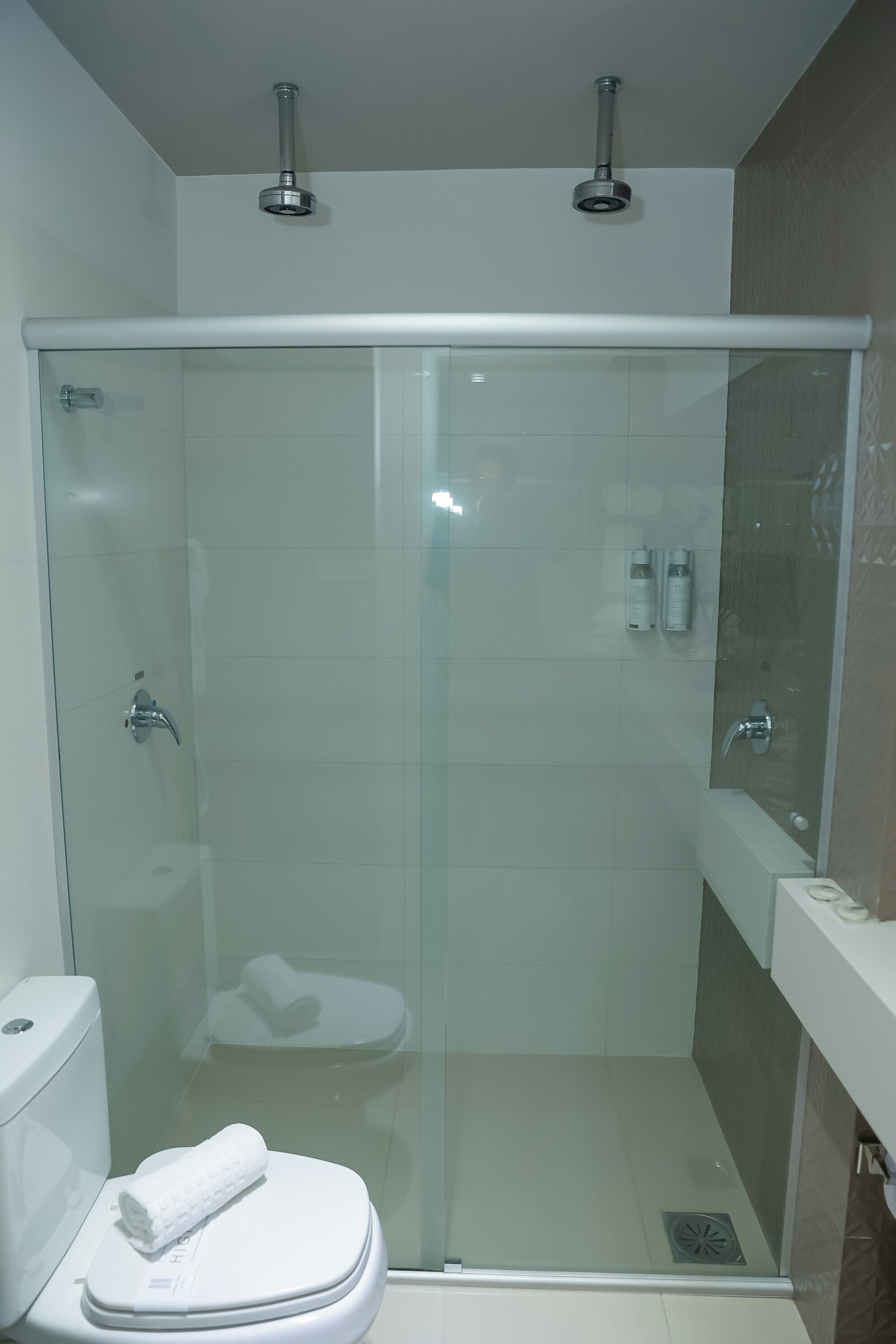 Ein modernes Badezimmer mit einer Glaskabinent Dusche, einer weißen Toilette und einem Waschtisch mit Spiegel.