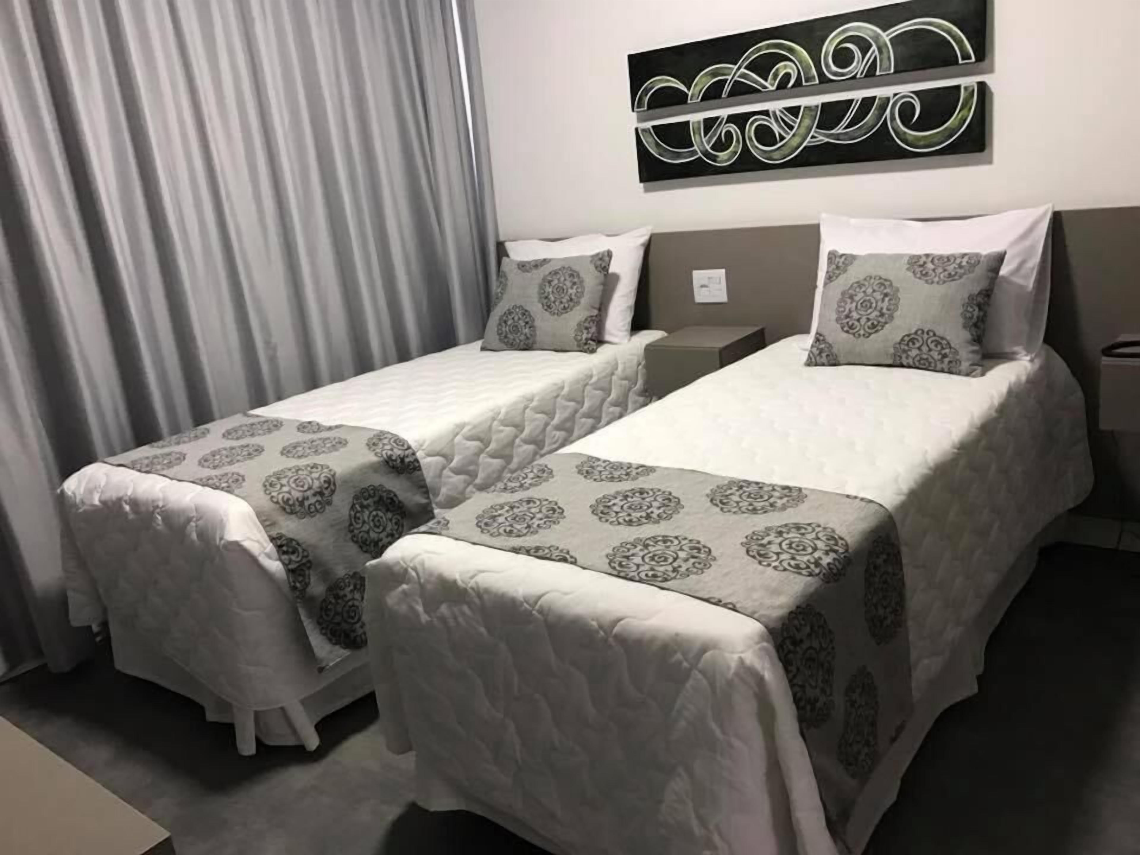 Habitación de hotel con dos camas, cada una con una colcha estampada y almohadas a juego. Incluye una cabecera con diseño decorativo, una mesita de noche y una obra de arte colgada en la pared sobre las camas.
