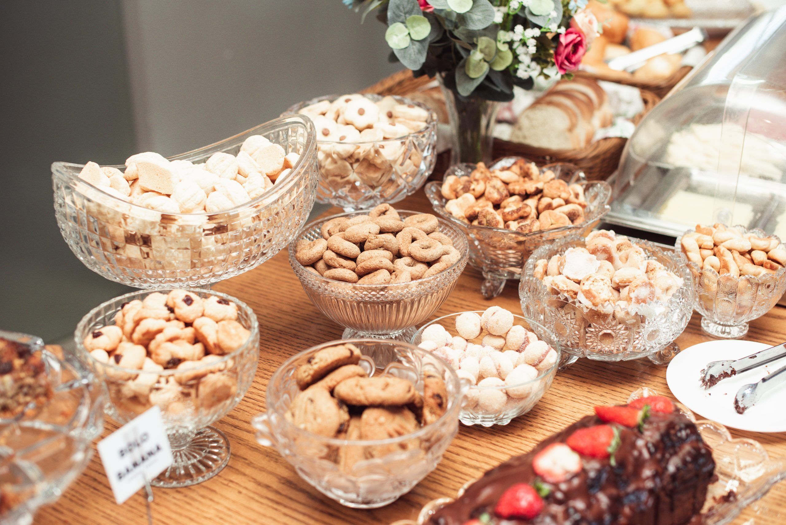 A buffet with various food items in glass bowls, including cookies, pastries, and a chocolate dessert.