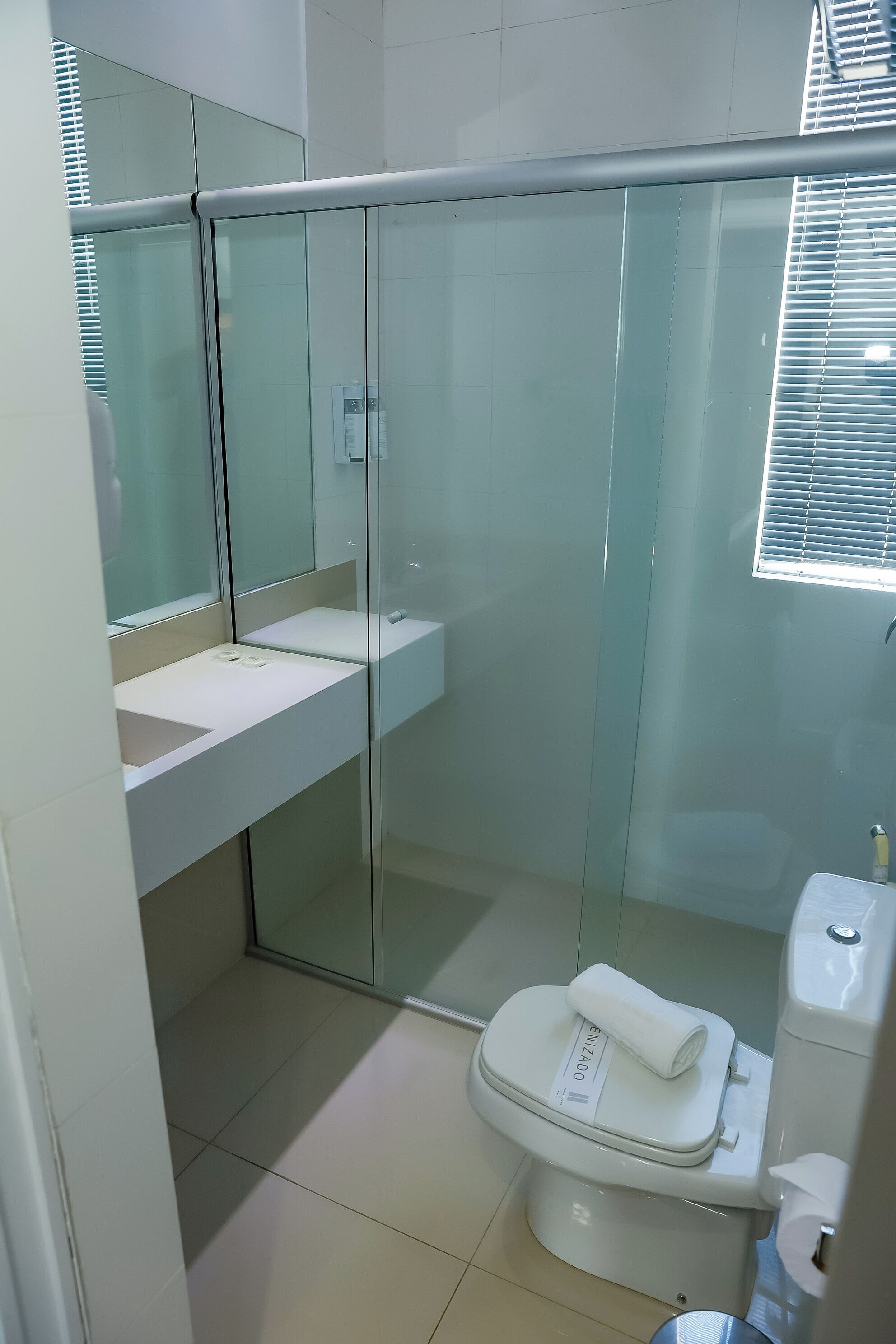 A modern bathroom with a glass-enclosed shower, a white sink, and a toilet with a towel on top.