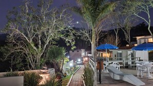 Un espace extérieur aménagé pour la nuit, avec un chemin pavé, des sièges et une fontaine.