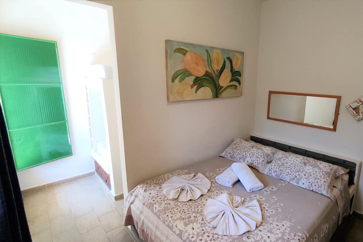 A bedroom with a bed, floral artwork, a mirror, and a green door.