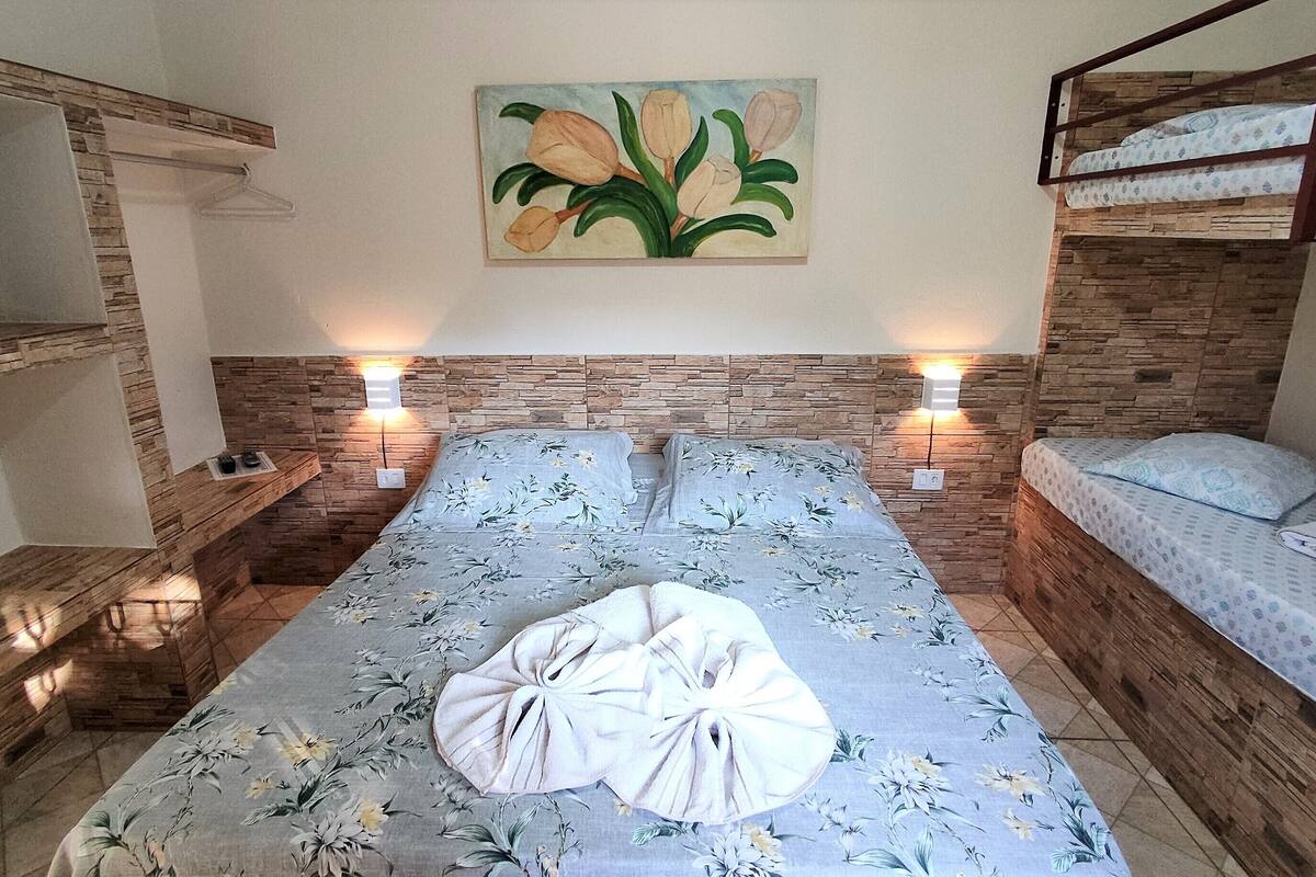 A bedroom with a floral bedspread, a painting of flowers on the wall, and a bunk bed on the right.