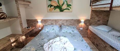 A bedroom with a floral bedspread, a painting of flowers on the wall, and a bunk bed on the right.