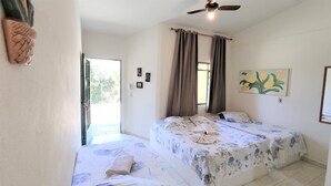 Une chambre avec deux lits, un ventilateur de plafond, une fenêtre avec des rideaux et un tableau au mur.