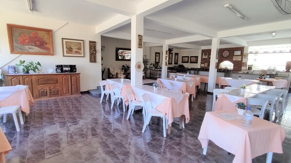 Un comedor con mesas y sillas, un aparador de madera y cuadros en las paredes.