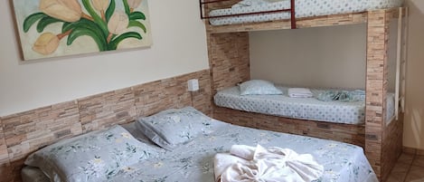 A room with a bunk bed, a single bed, floral bedding, a painting of flowers, and a stone-patterned wall.