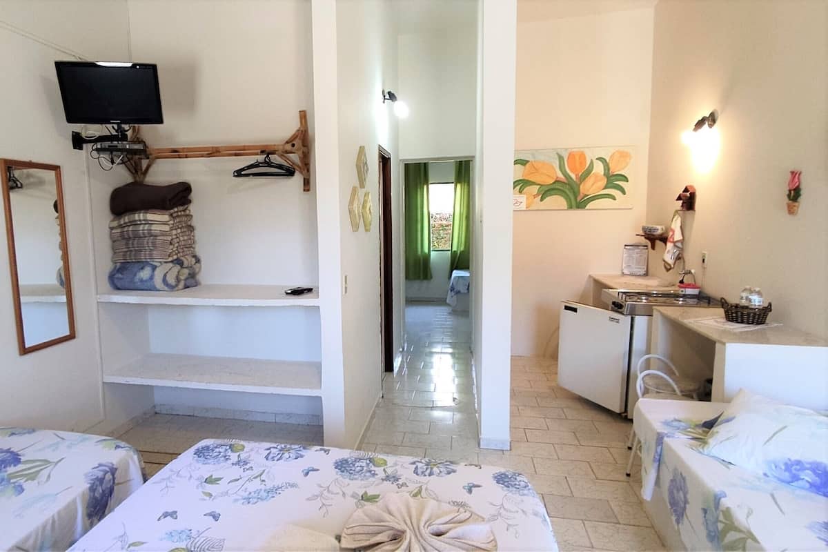 A hotel room with two beds, a TV, a desk with a computer, a small fridge, and a hallway leading to another room.