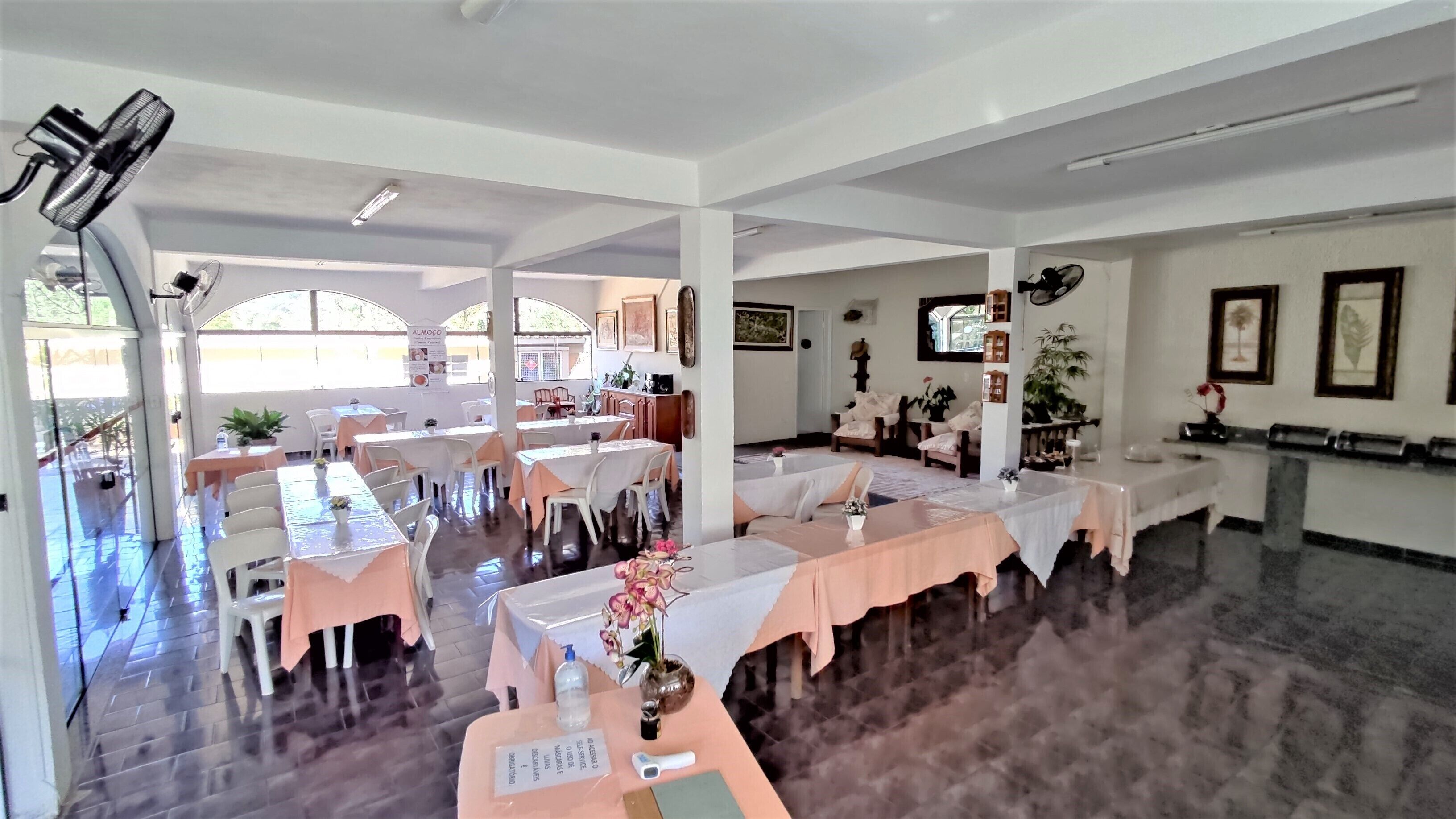 A spacious indoor dining area with multiple tables and chairs, large windows, and a ceiling fan.