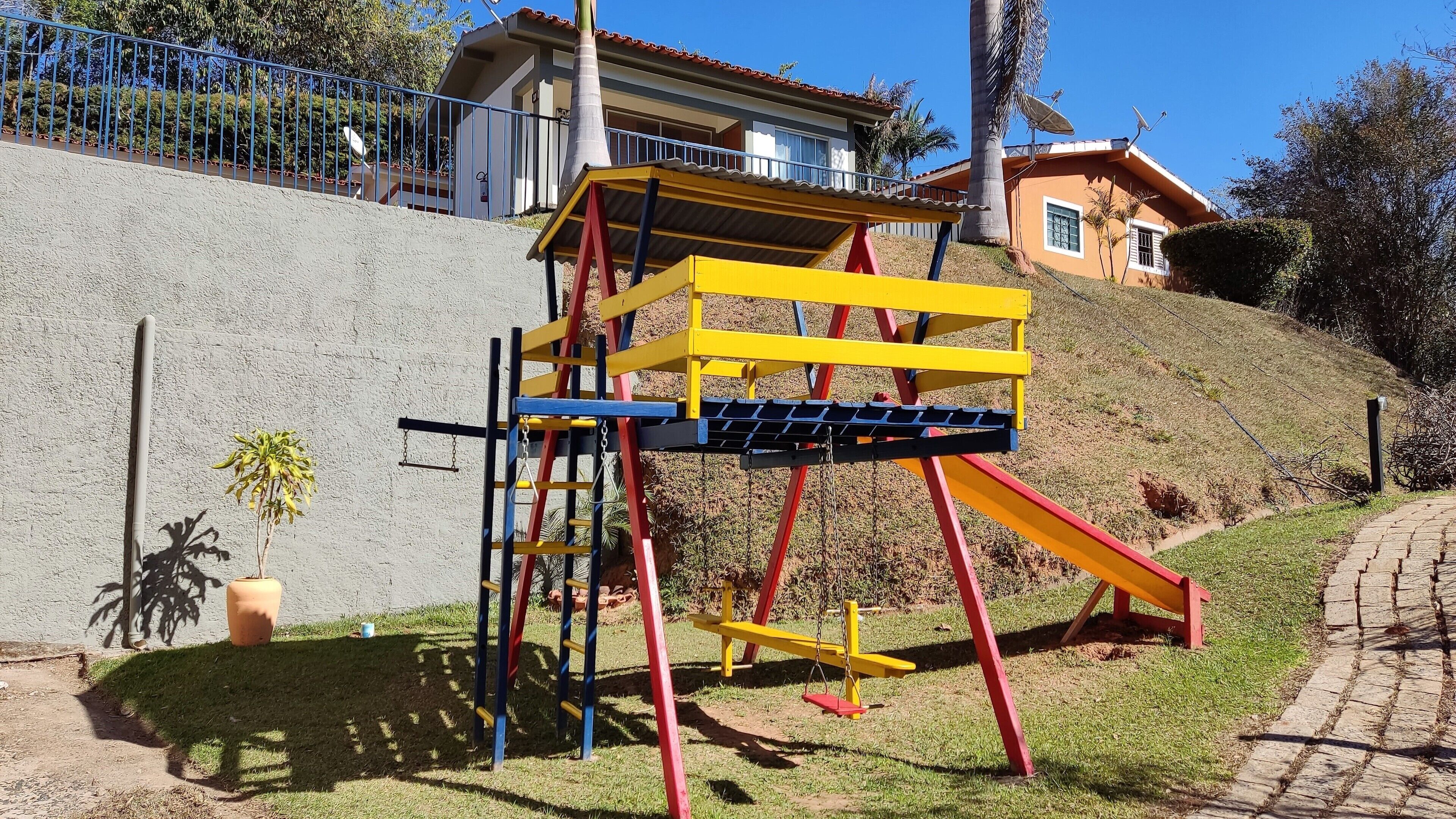 A playground with a yellow and red climbing structure, a small potted plant, and a paved path.