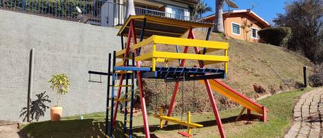 A playground with a yellow and red climbing structure, a small potted plant, and a paved path.