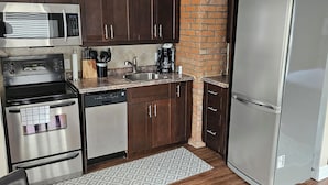 Une cuisine moderne dotée d’appareils électroménagers en acier inoxydable, de meubles de rangement en bois foncé et d’un mur décoratif en briques.