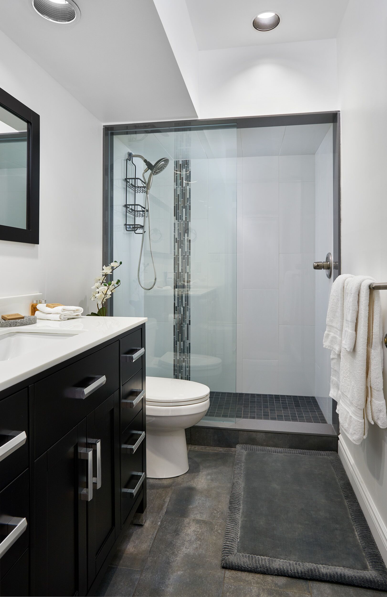 Une salle de bain moderne avec une douche à parois de verre, des toilettes blanches et un meuble-lavabo noir doté de tiroirs.