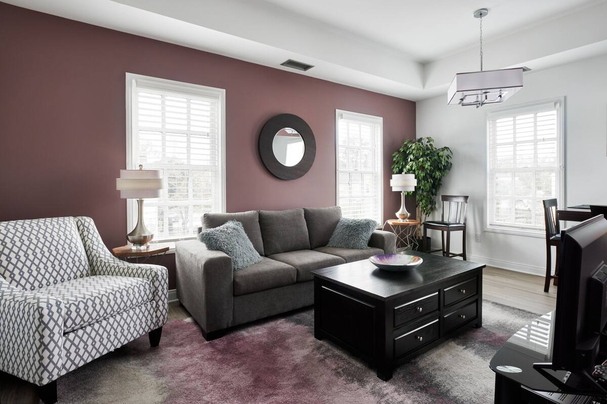 Un salon avec un canapé gris, un fauteuil à motifs et une table basse noire.