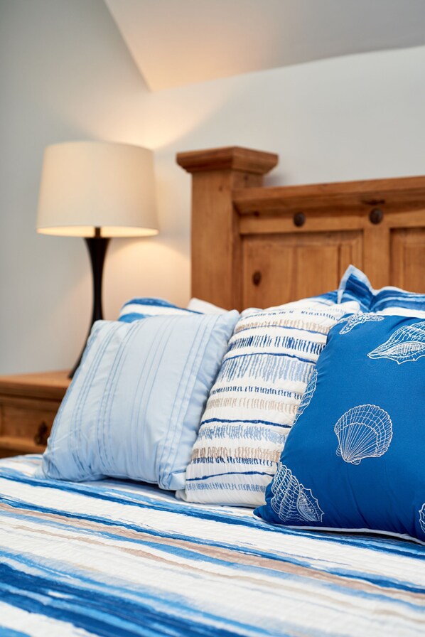A bed with striped bedding and multiple pillows, including a blue one with shell patterns.