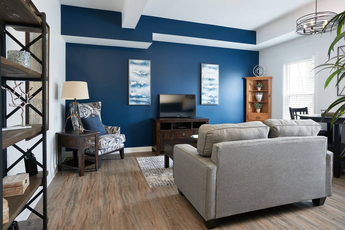 Un salon avec un mur d’accent bleu, un canapé, un téléviseur et une bibliothèque en bois.