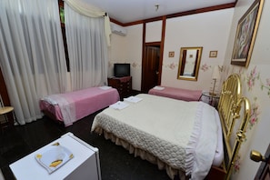 Quarto de hotel com duas camas, televisão, escrivaninha com cadeira e janela com cortinas.