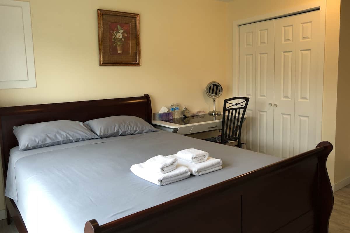 A neatly made bed with pillows, a bedside table with a lamp, a chair, and a door.