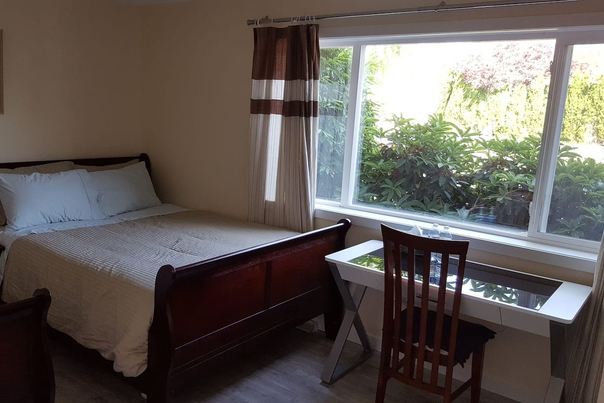 A bedroom with a bed, bedside table, lamp, and a desk with a chair.