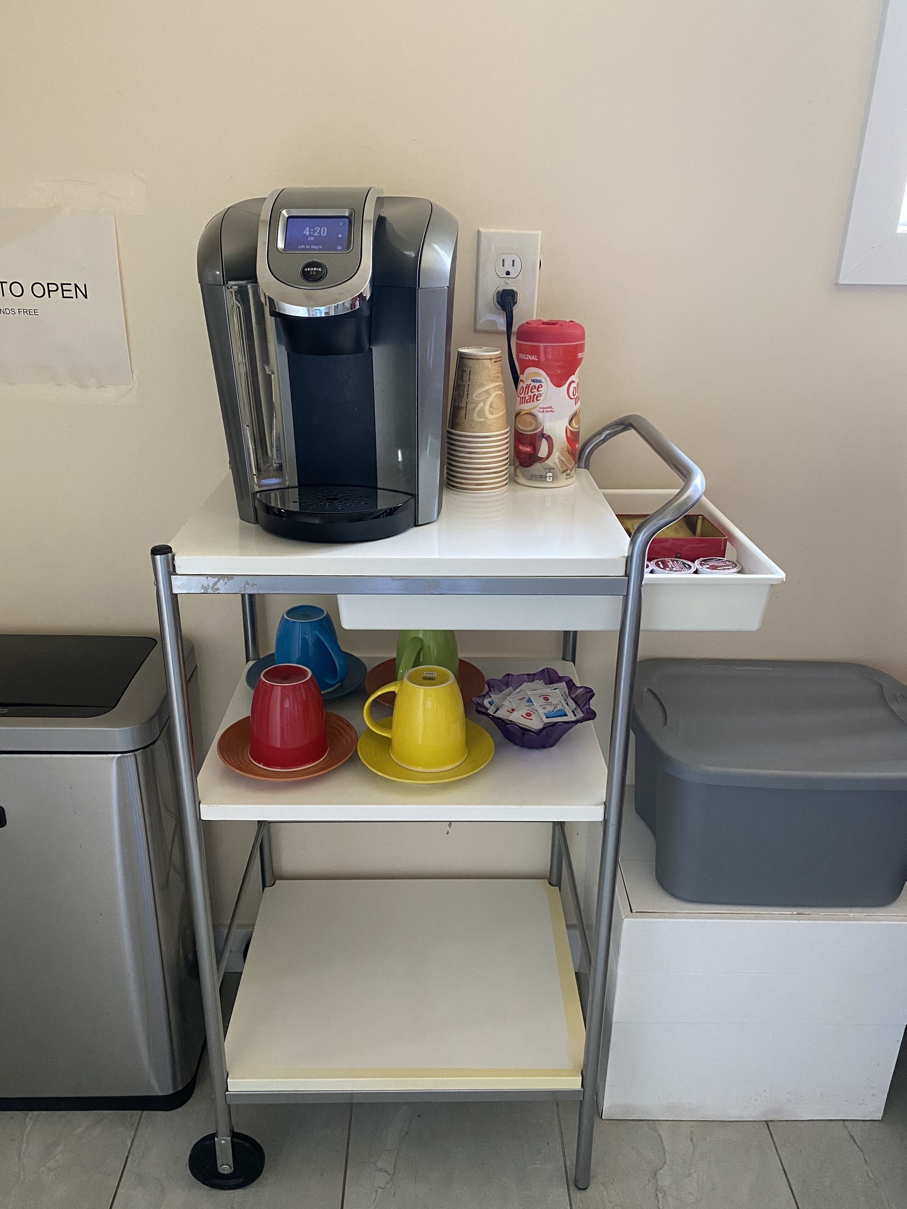 A coffee station with a coffee maker, disposable cups, and a coffee mug.
